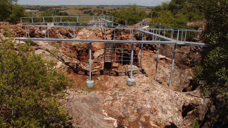 A network of elevated metal walkways rings a rocky pit.