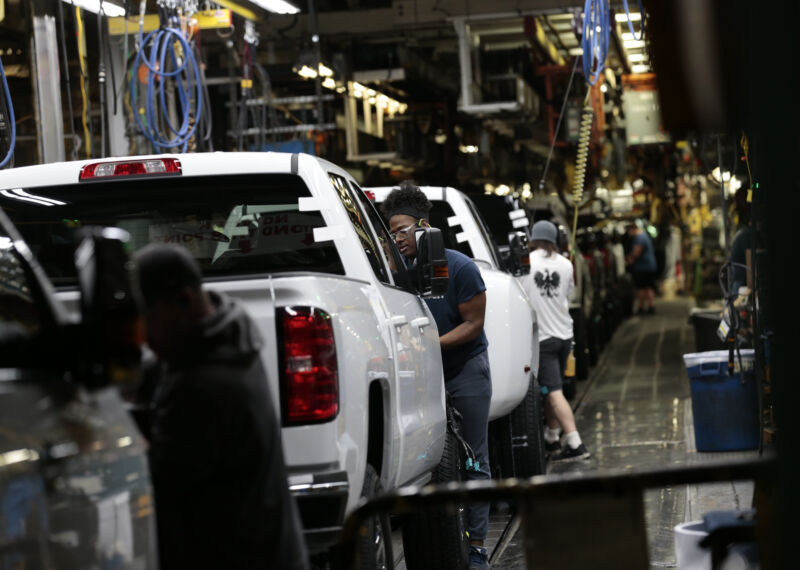 People in light protective gear work on trucks.