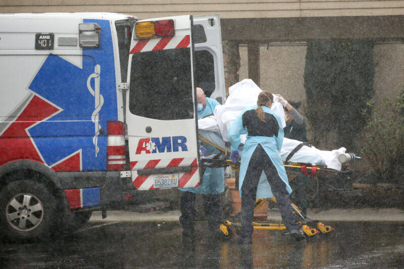 People in protective clothing load a stretcher-bound patient into an ambulance.