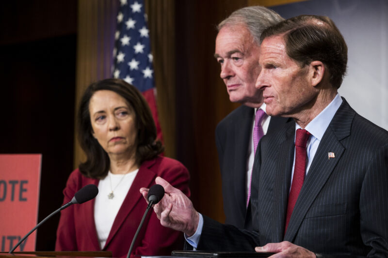 Serious people in suits stand at a podium with a microphone.