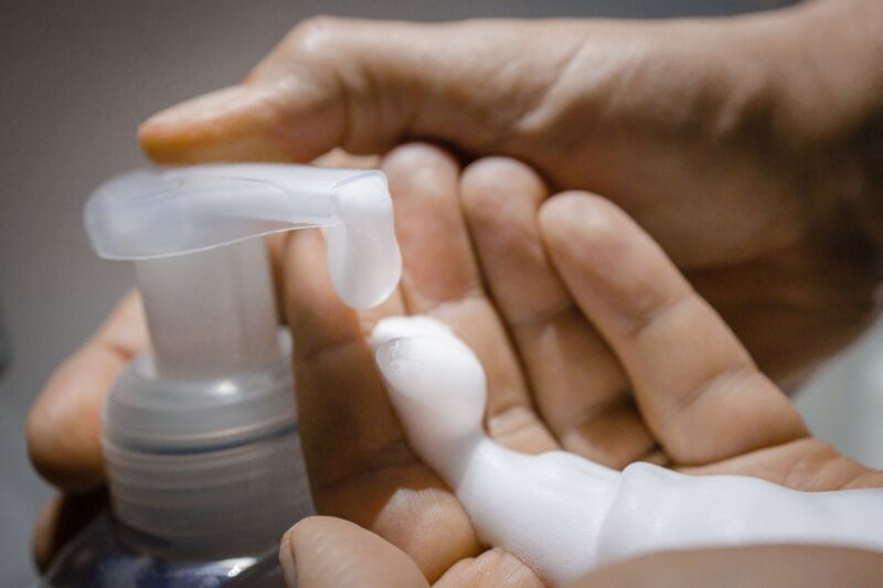 A person washing their hands with a bottle of soap.