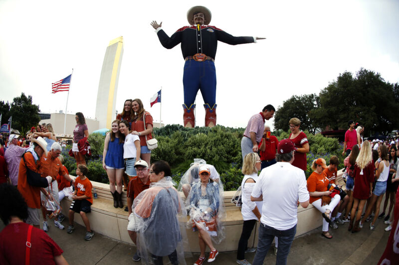 Casually dressed people congregate around an oddly misshapen humanoid statue.