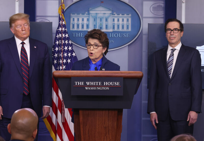 Three people stand by a podium in front of the White House logo.