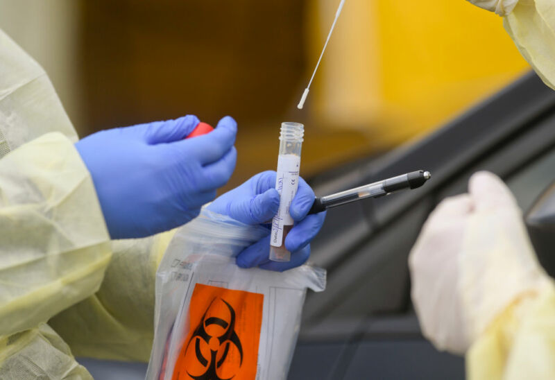 Bern twp., PA—March 27: A registered nurse puts a nasal swab into a tube held by another nurse, both wearing gloves and protective gowns, after doing a nasal swab on a patient in their car at Penn State Health St. Joseph.