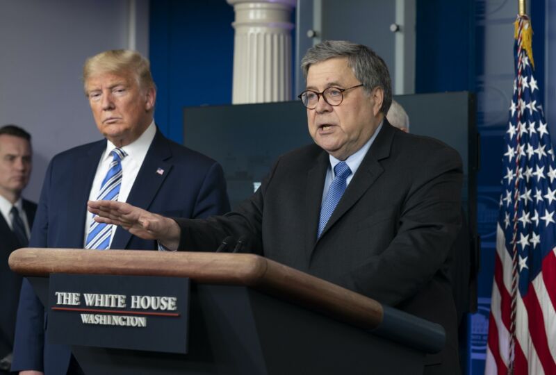 Attorney General William Barr speaking at a podium while President Trump looks on.