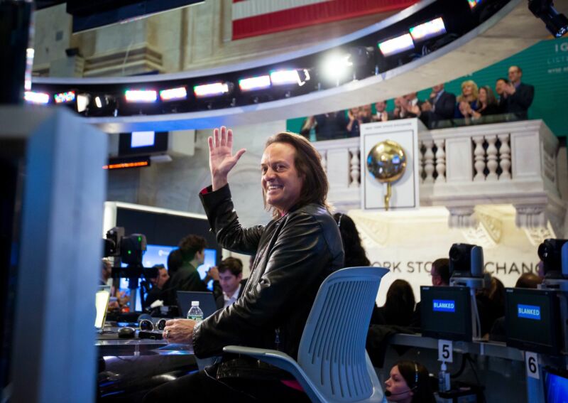 Le PDG de T-Mobile, John Legere, est assis sur une chaise et salue la caméra.