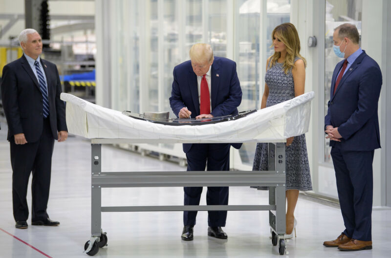 President Trump signs an Orion capsule hatch that will be used for the Artemis II mission as Vice President Mike Pence, First Lady Melania Trump, and NASA Administrator Jim Bridenstine (wearing a mask) look on.