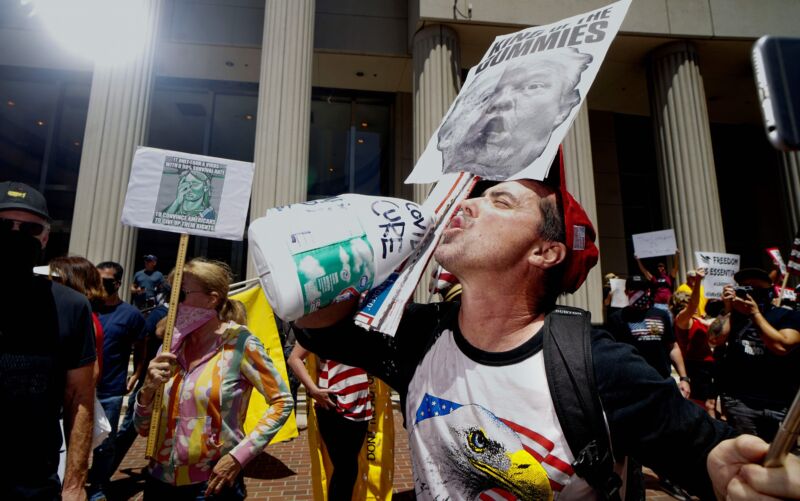 A demonstrator holding an anti-Trump sign pretends to drink from a bottle of bleach during a rally to re-open California and against Stay-At-Home directives on May 1, 2020 in San Diego, California.