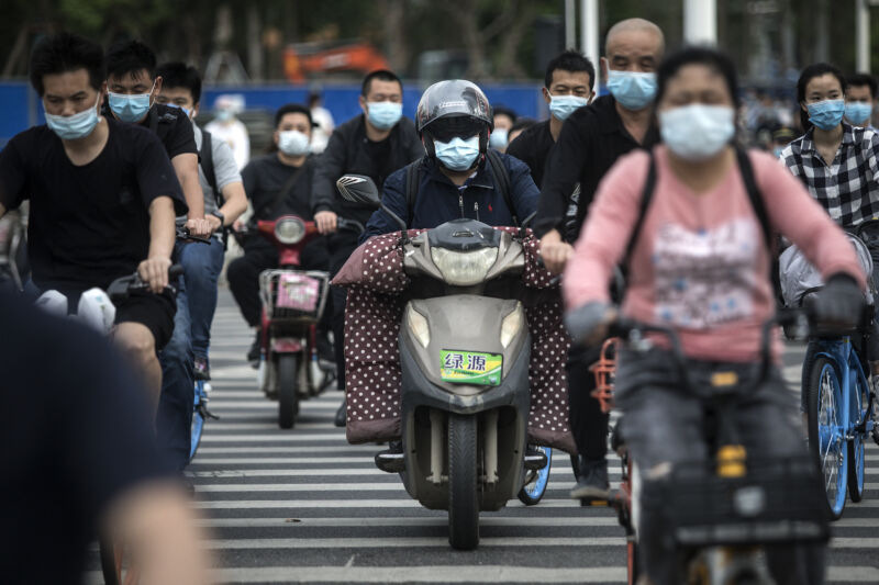 A road is full of masked people on scooters and bikes.