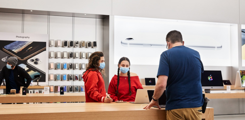 Masked retail workers stand across a counter from a customer.