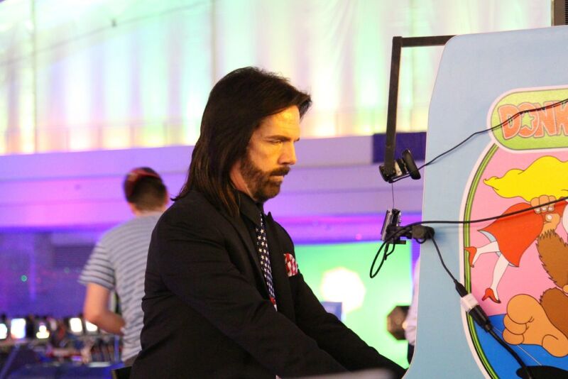 A long- haired man plays in a video game cabinet from the late 70s/early 80s.