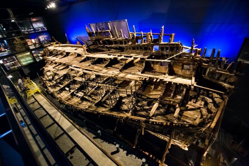 An ancient wooden hull is housed in a vast room.