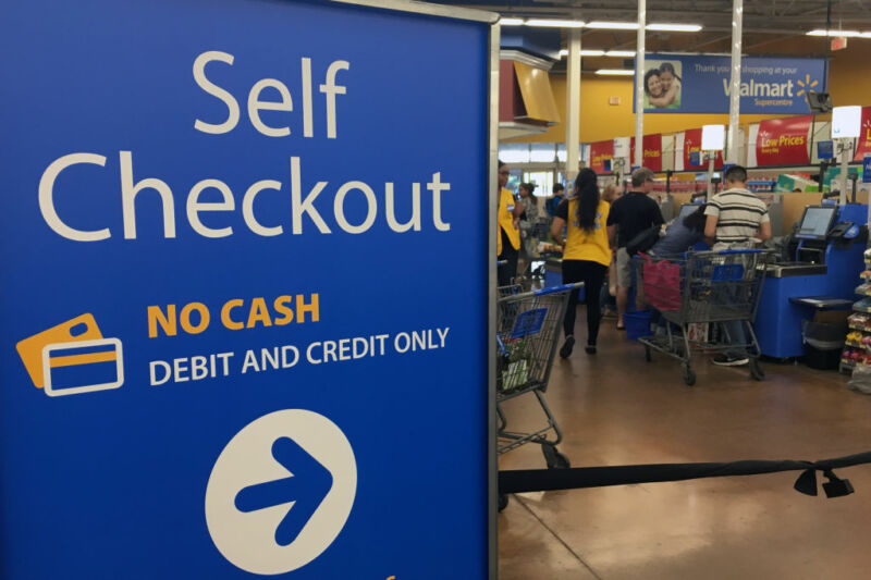 Customers and staff cluster around grocery store self-check lane.