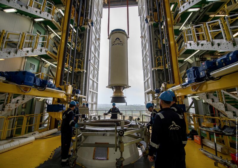 People In Hardhats Stand Around A Rocket.