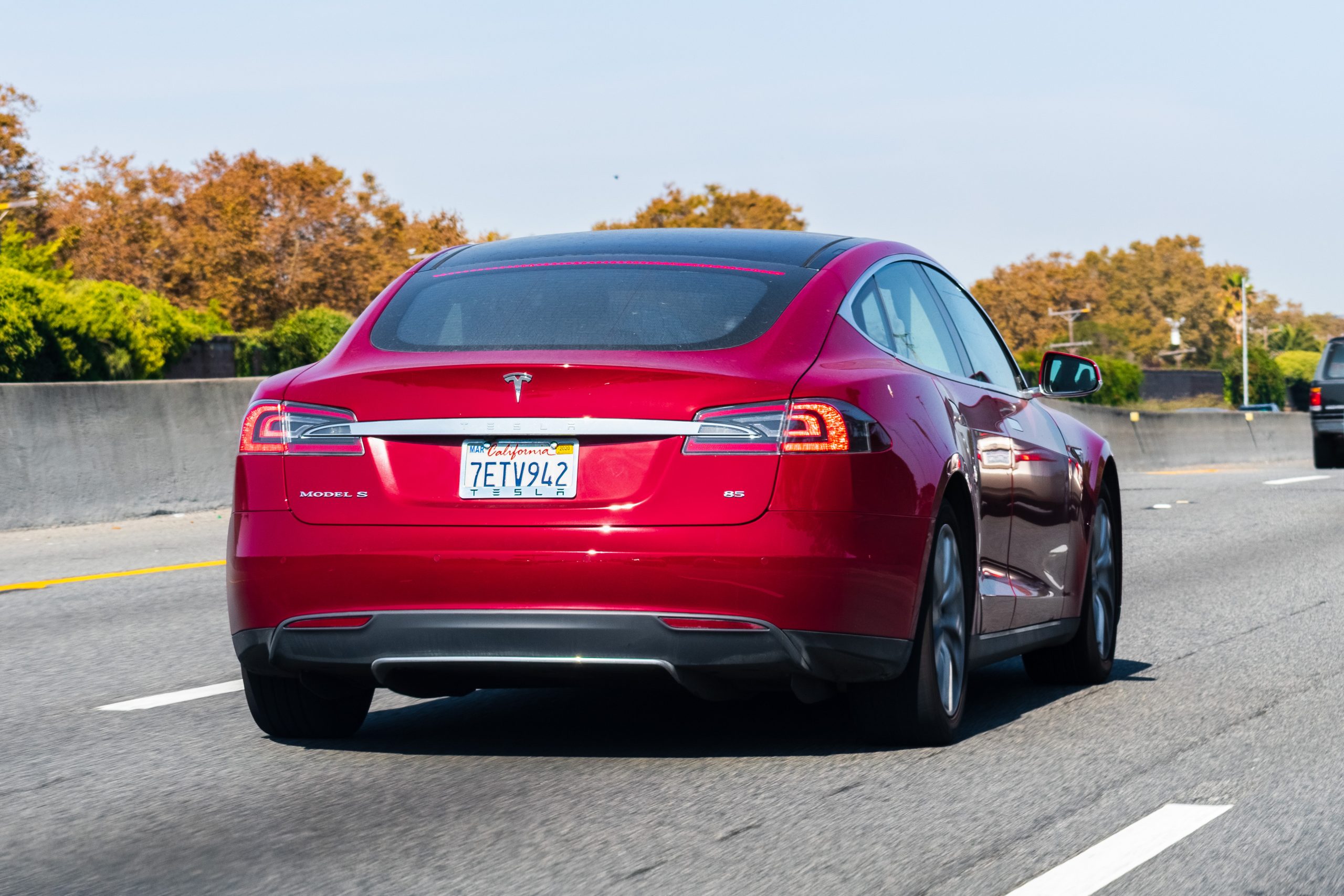 A red sedan cruises down a tree-lined highway.
