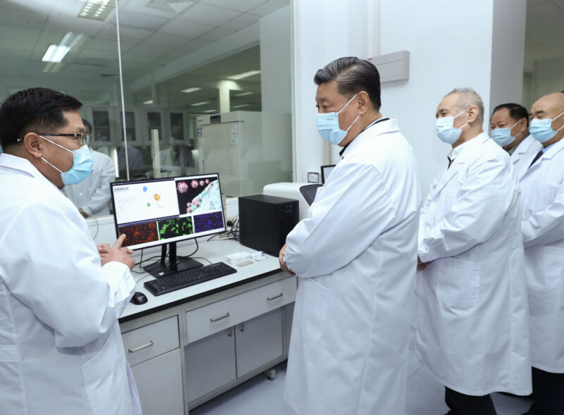 Men in white lab coats and face masks talk amongst themselves.