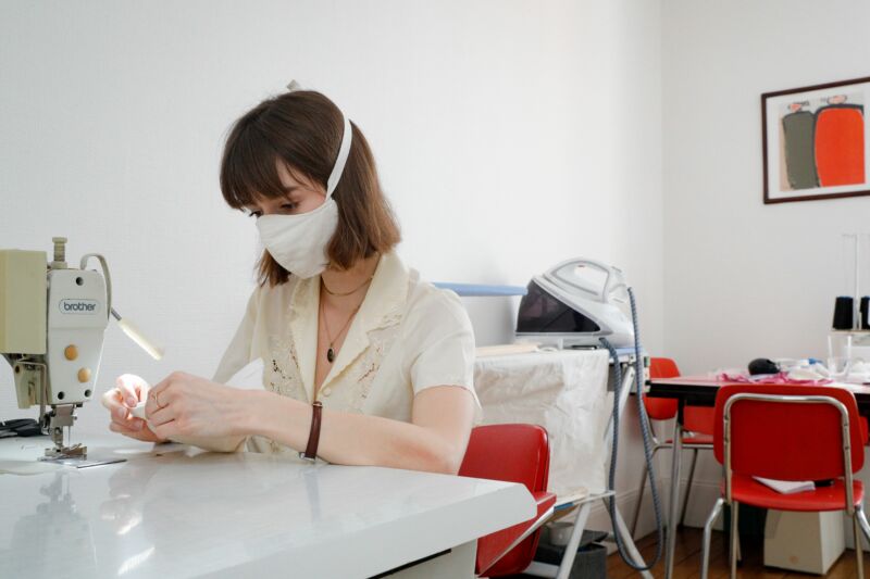 A masked woman operates a sewing machine.
