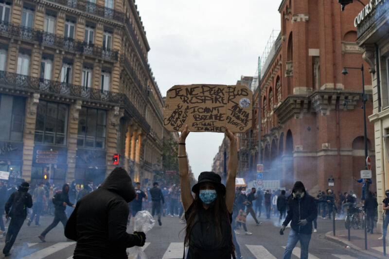 A woman holds a placard reading 'I can't breathe' amid tear gas in Toulouse, France.