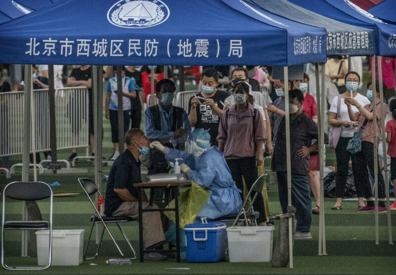 Masked people line up to have swabs stuck in their faces.