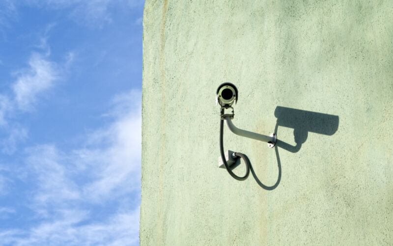 A surveillance camera mounted on a wall on a sunny day.