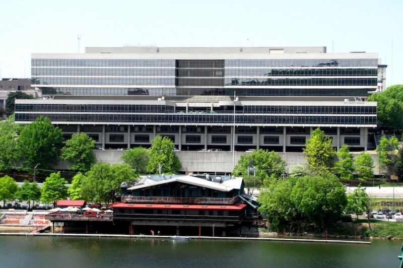 A modern, multistory glass building overlooks a river.