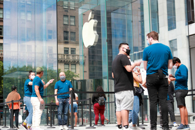 Masked people mill about the glass walls adorned with the Apple logo.