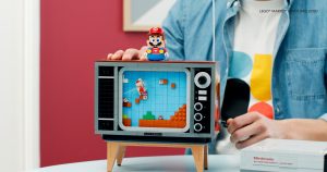 A person turns the handle on the side of the Lego TV set to make Mario scroll