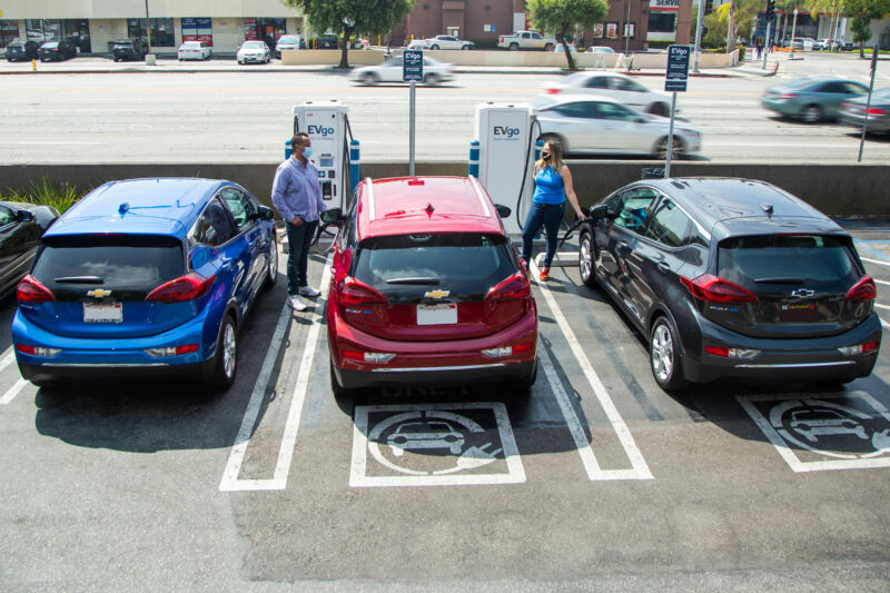 Two masked, socially distanced people charge their electric cars.