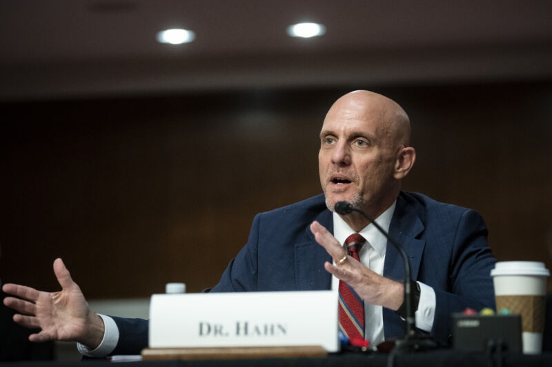 A serious man in a business suit speaks into a microphone.