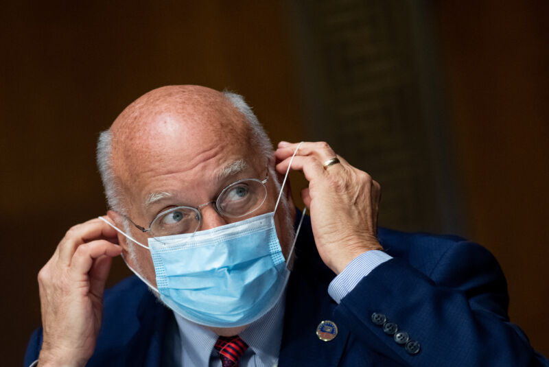 A serious man in a business suit puts on a surgical mask.