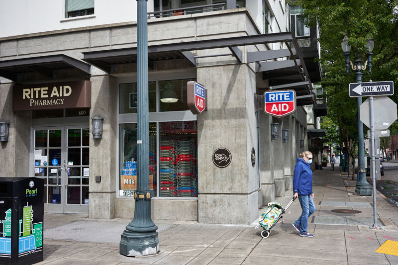 A masked woman pulls a cart on an urban street corner.