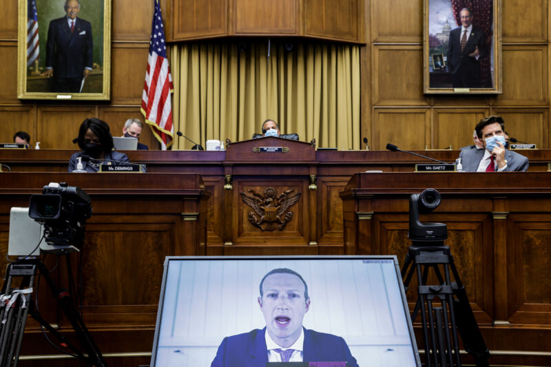 Masked legislators listen to a man on a computer screen.