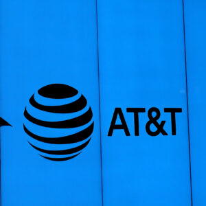 A man with an umbrella walking past a building with an AT&T logo.