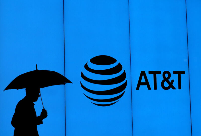 A man with an umbrella walks past a building with an AT&T logo on it.