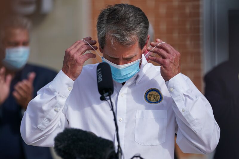 Georgia Governor Brian Kemp putting on a mask at a public event.