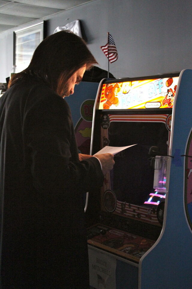 Billy Mitchell reviews a document in front of a <em>Donkey Kong</em> machine decked out for an annual "Kong Off" high score competition.