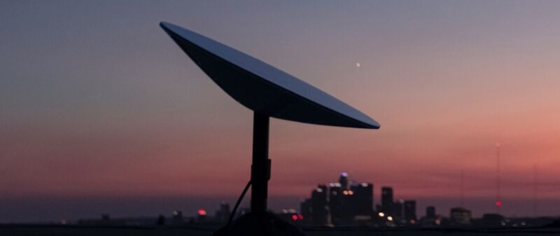 A SpaceX Starlink user terminal, also known as a satellite dish, seen against a city's skyline.