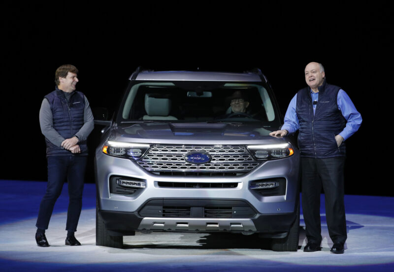 Two men in business casual stand next to an SUV.