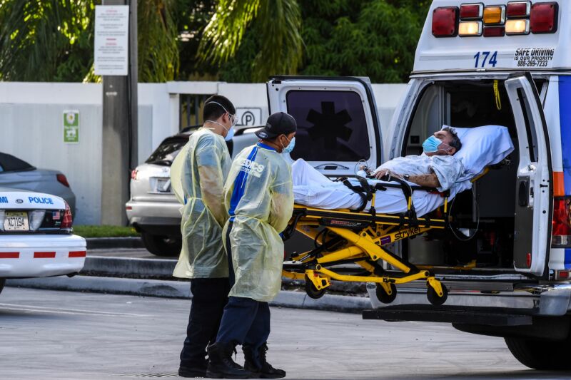 Health workers in protective gear move a masked patient into the back of an ambulance.