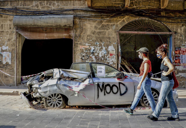 Women walk past a damaged car on August 13, a week-plus after the Port of Beirut explosions. Getty's suggested caption describes the streets of Beirut as "just like war zones with the destroyed buildings, shattered roads, smelly garbages scattered almost everywhere." 