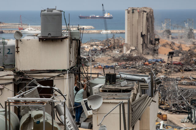 A man tries to fix an electricity cable on the damaged roof of an apartment block facing the Beirut port on August 13, 2020.