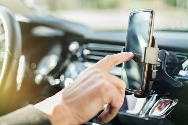 A man's hand tapping a smartphone in a car.