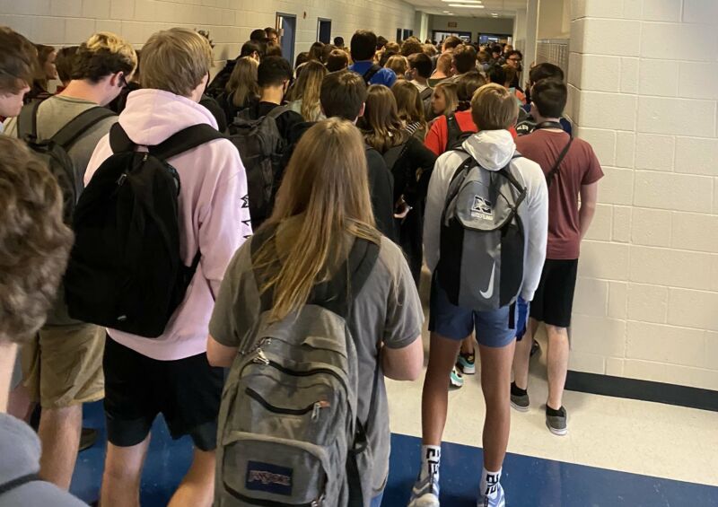 A photo of high school students in a hallway between classes, with kids packed closely together and many not wearing masks.