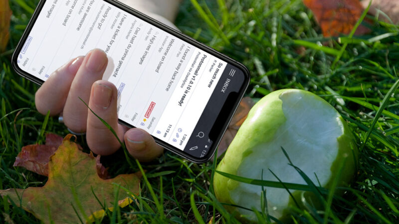 Closeup photograph of a hand holding a smartphone up to a half-eaten apple.