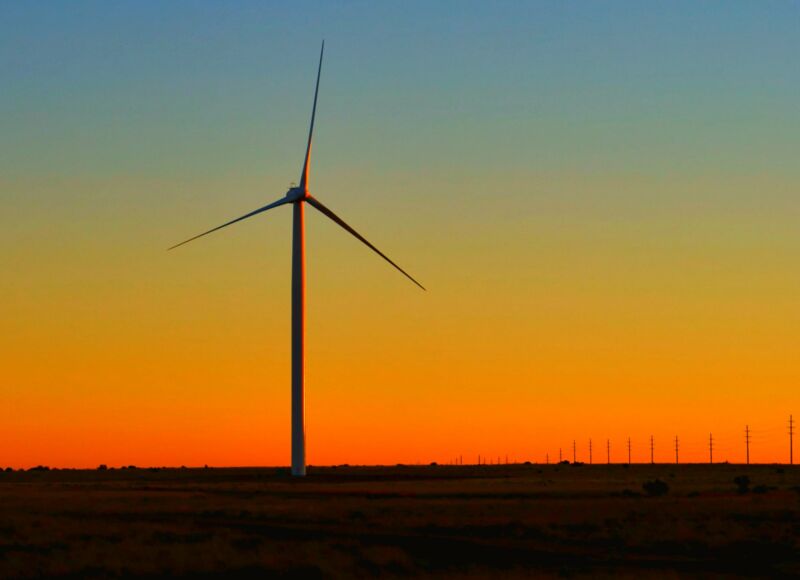 A wind turbine is silhouetted against the sunset.