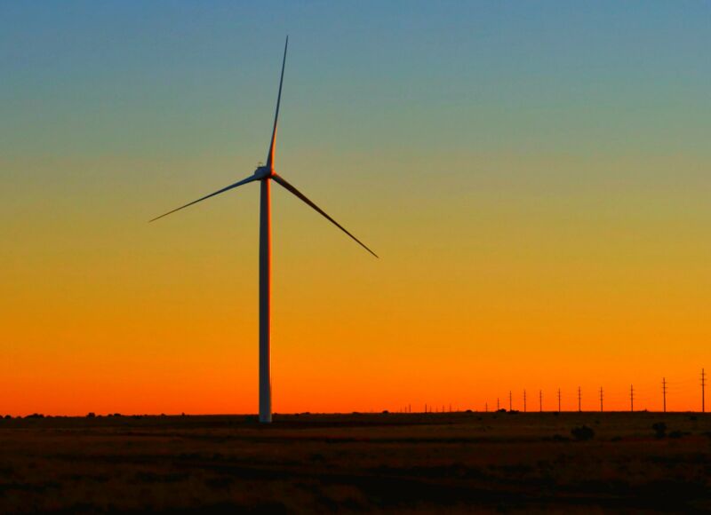 A Wind Turbine Is Silhouetted Against The Sunset.