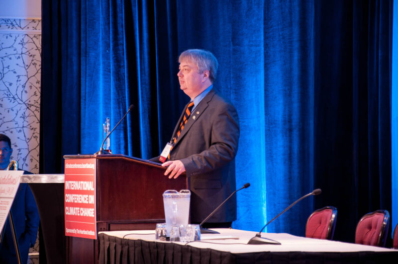 A man in a suit speaks at a podium.