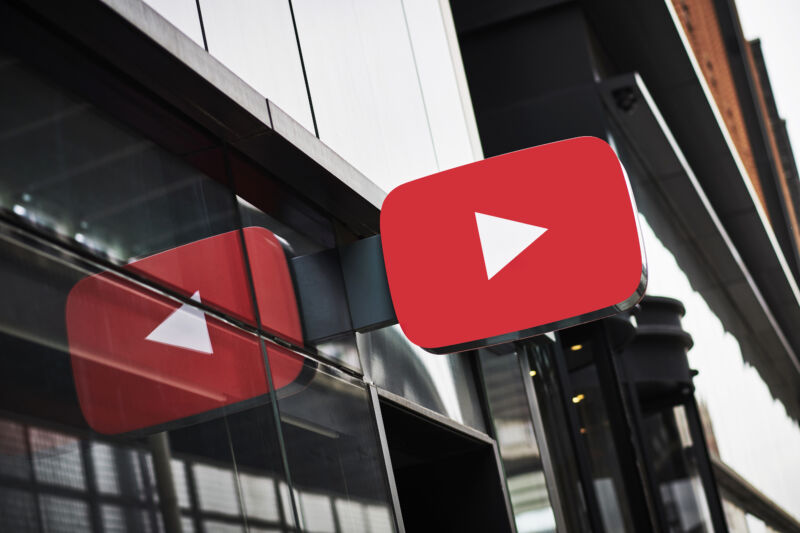 A sign in the shape of the YouTube logo juts out over a glass wall.