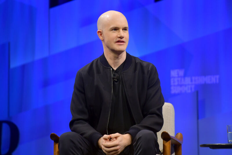 A Casually Dressed Man Speaks From A Chair Onstage.