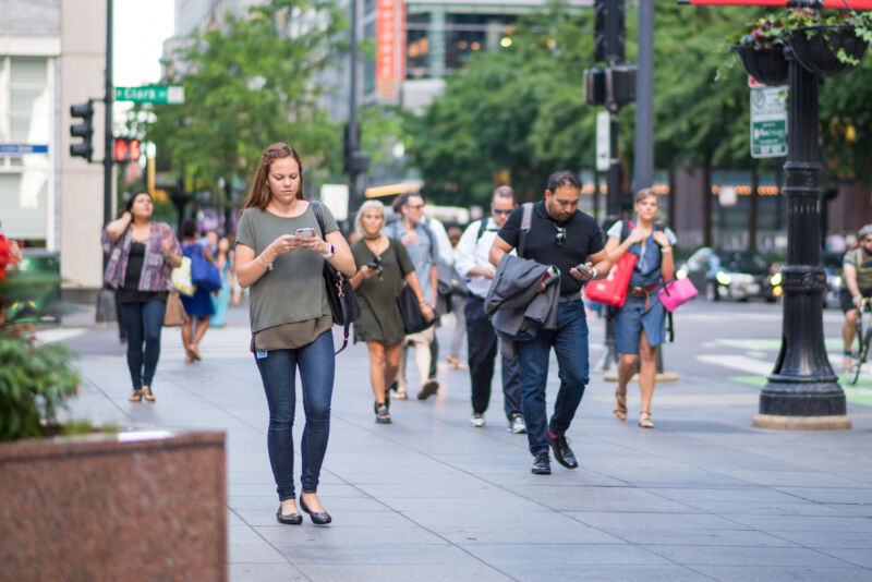 Stock photo of people on urban sidewalk walking and looking at smartphones.